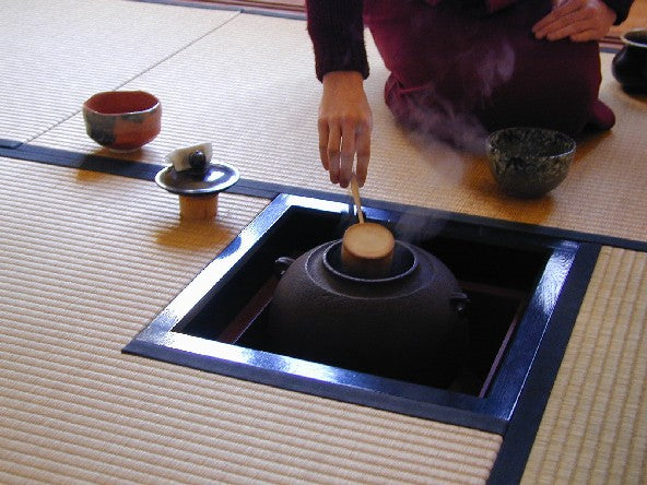 Japanese ro hearth with iron kama supported above the charcoal fire, illustrating the gotoku trivet concealed in the ash