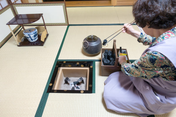 Japanese tea ceremony charcoal being handled with long hibashi-style fire chopsticks over a hearth