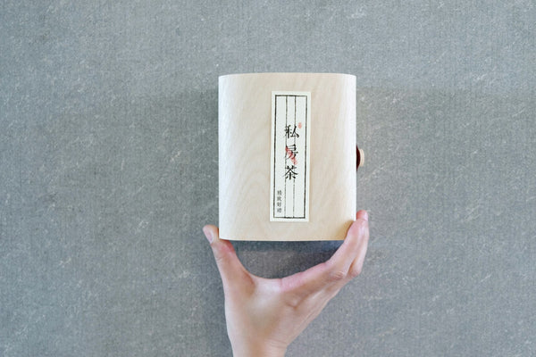 Hands holding a wooden box marked with Japanese writing