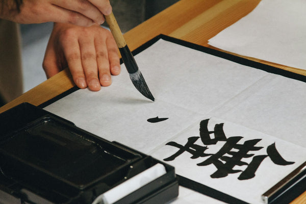 Brush writing Japanese characters in black ink on white paper