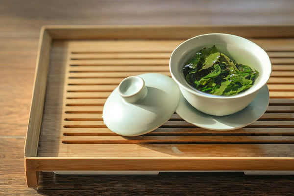 Loose green tea leaves in a white ceramic bowl