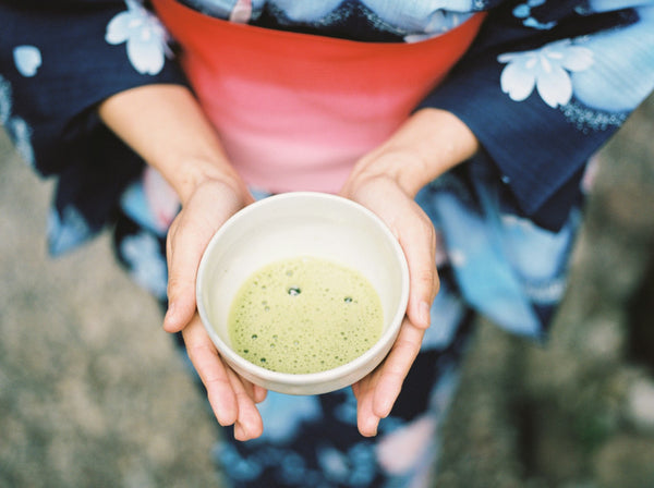 Person carefully holding a ceramic bowl during a matcha tea setting