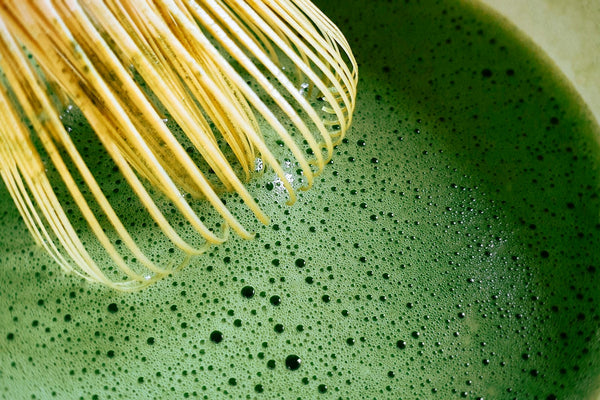 Bamboo chasen whisking bright green matcha in a ceramic bowl
