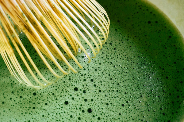 Bamboo chasen whisking bright green matcha in a bowl
