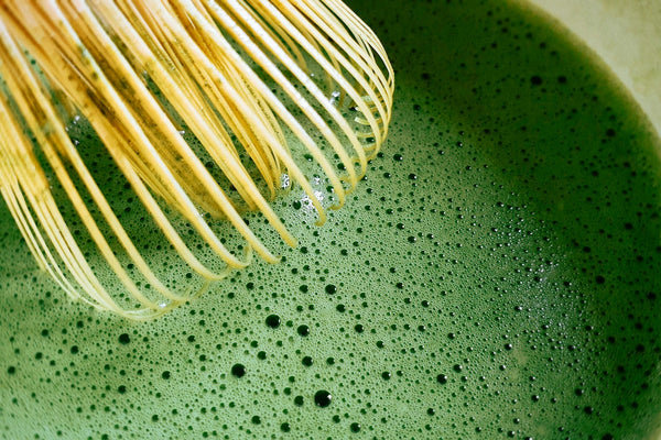 Bamboo chasen whisk preparing bright green matcha in a tea bowl