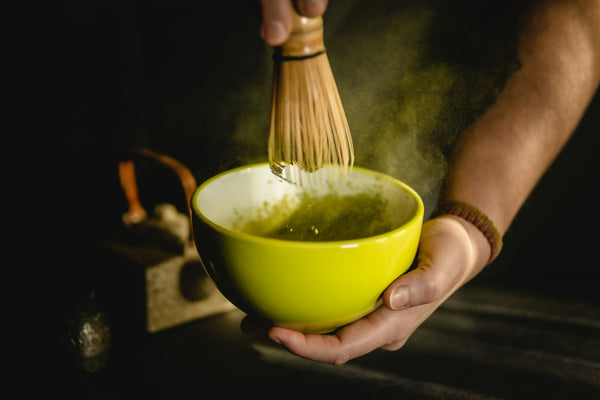 Hands holding a green ceramic bowl of matcha