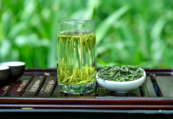 Glass of green tea beside loose green tea leaves