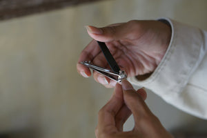 A person trimming a fingernail with a handheld nail tool