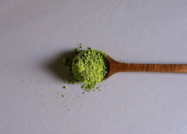 Bright green matcha powder on a wooden scoop