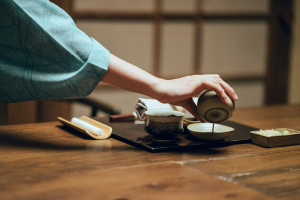 Person pouring tea into a cup at a wooden table