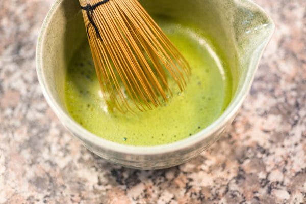 Foamy matcha being whisked in a ceramic bowl with a bamboo chasen