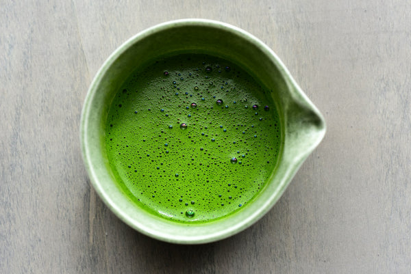 Prepared matcha in a green ceramic bowl on a wooden surface