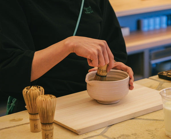 Hands whisking matcha in a ceramic tea bowl