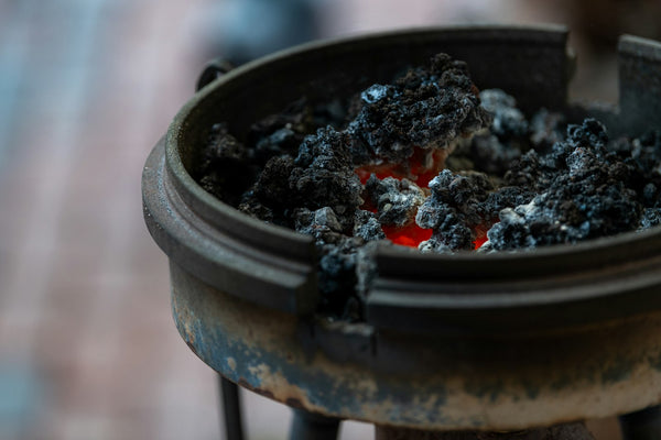 Glowing charcoal embers and pale ash inside a dark brazier