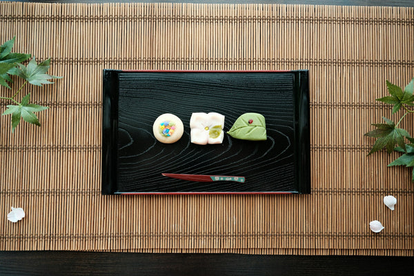 Japanese sweets arranged on a dark serving tray with a small sweet pick, illustrating kashiki-style sweets presentation