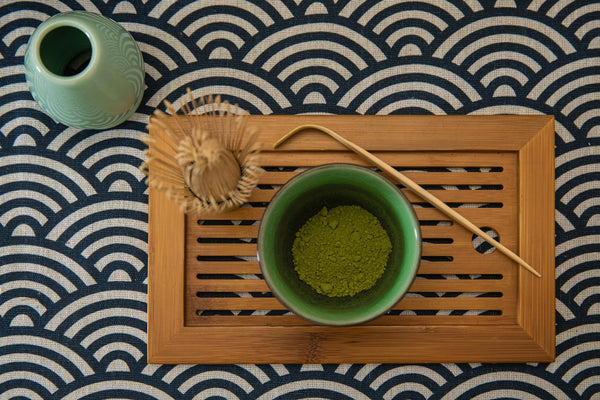 Matcha powder with bamboo whisk and scoop arranged on a wooden tray