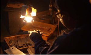 Knife maker inspecting a kitchen knife blade under a work light