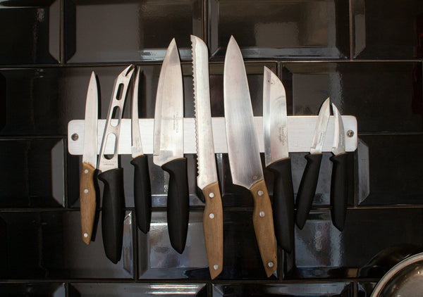 Several kitchen knives stored together on a magnetic wall strip