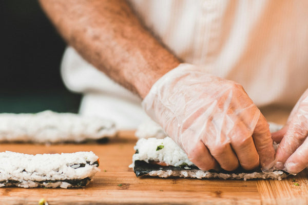 Hands preparing sushi at a work surface with a slicing knife